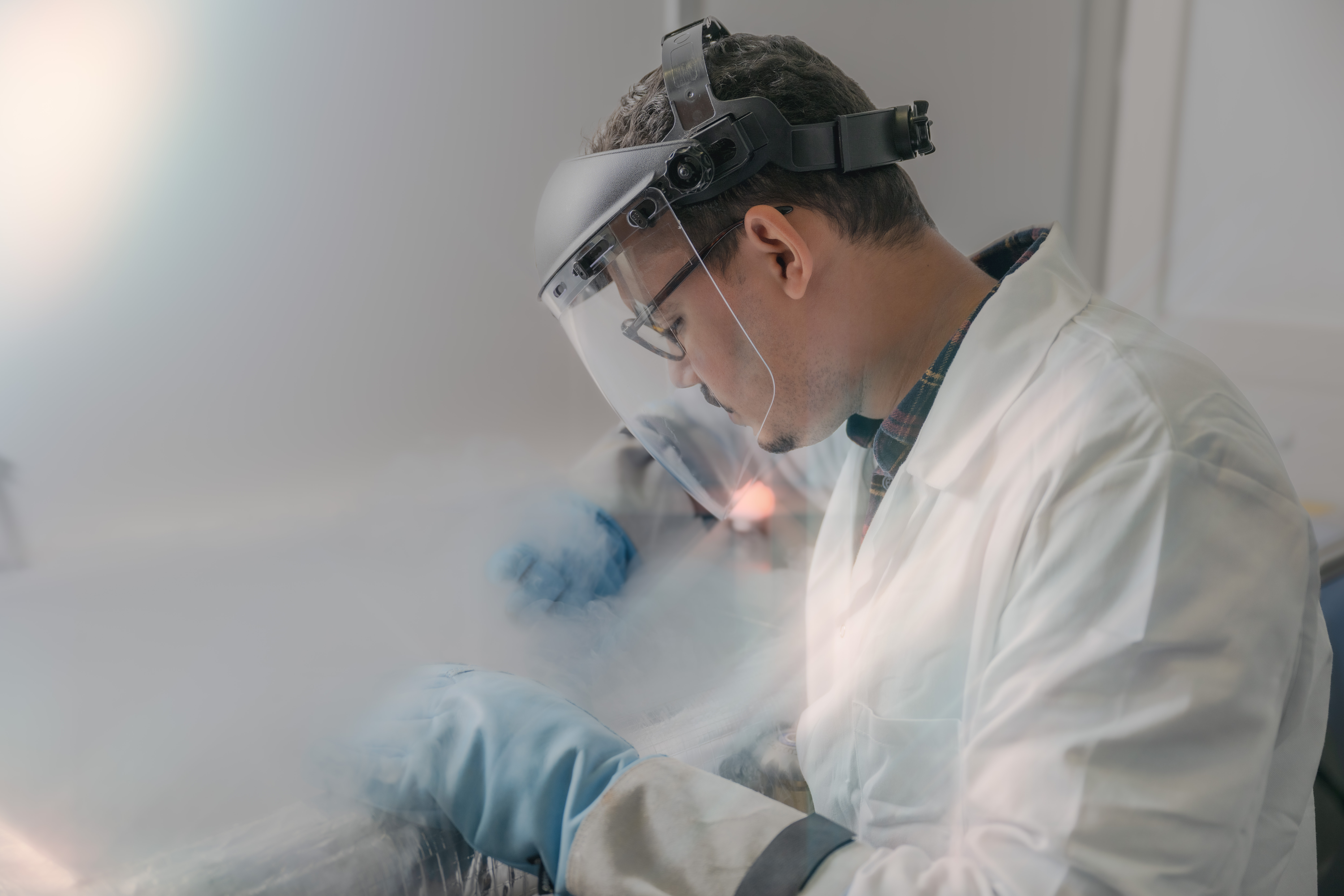Engineer in a white lab coat and wearing gloves working with cryogenics.